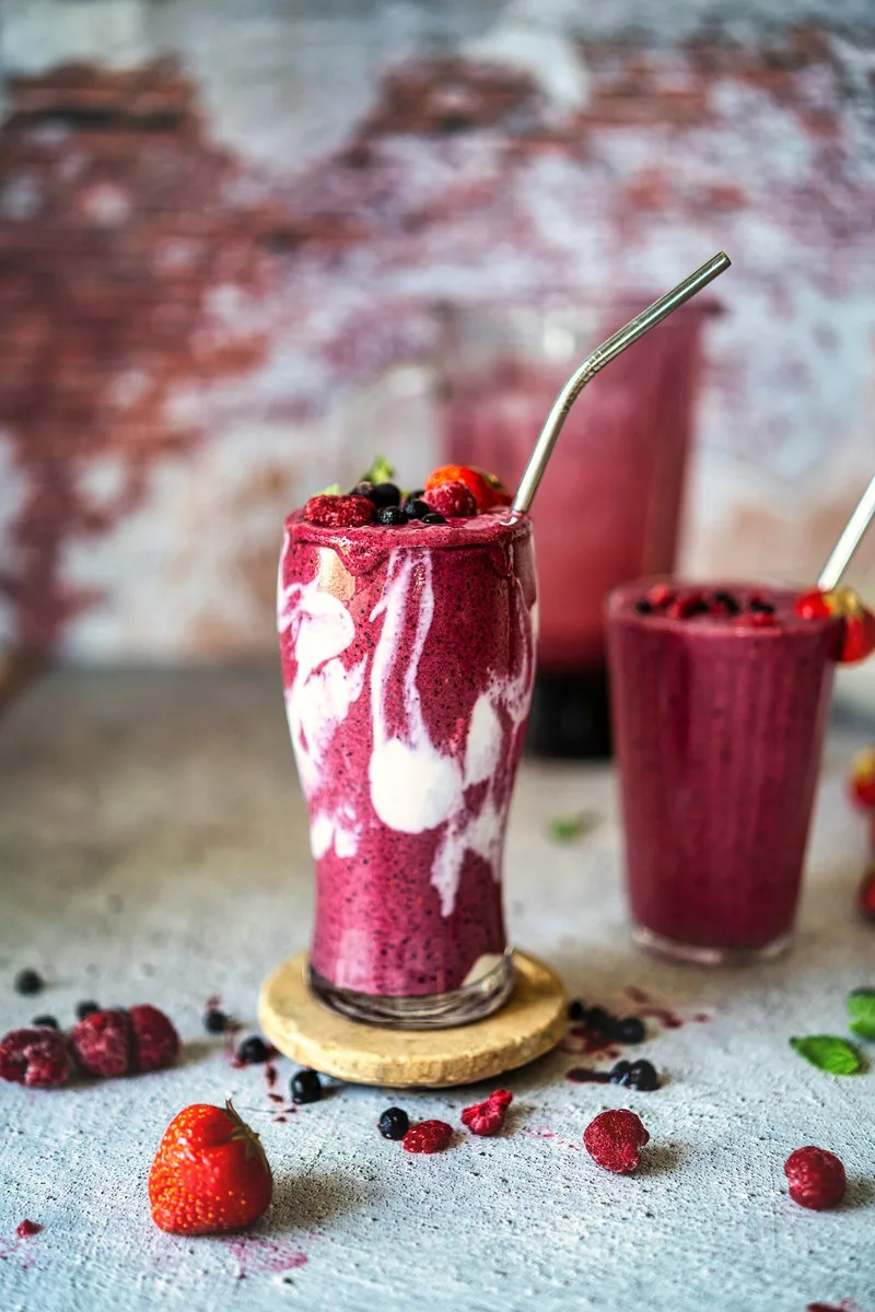 Fertiger Beerensmoothie im transparenten Glas mit Beeren daneben