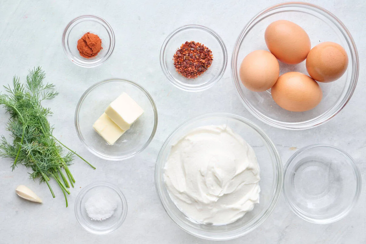 Ingrédients pour le çılbır turc : yaourt, ail, œufs, beurre, paprika et piment préparés pour la recette.
